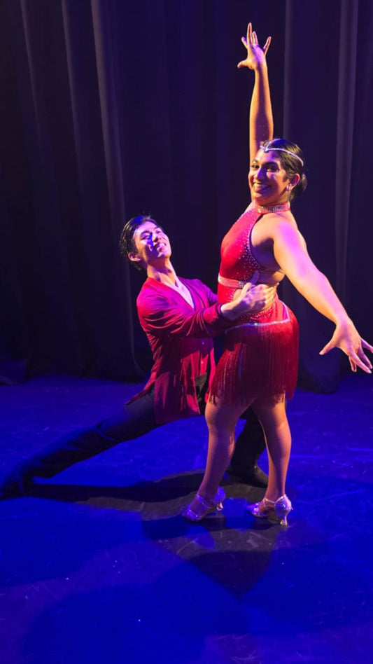 Avanka and Naoya, winners of the It Takes Two dance challenge winning two pairs of Mira Threads Fishnet Tights. They are posing in maroon costumes with Avanka standing 4th position and Naoya luging towards her holding her hips.