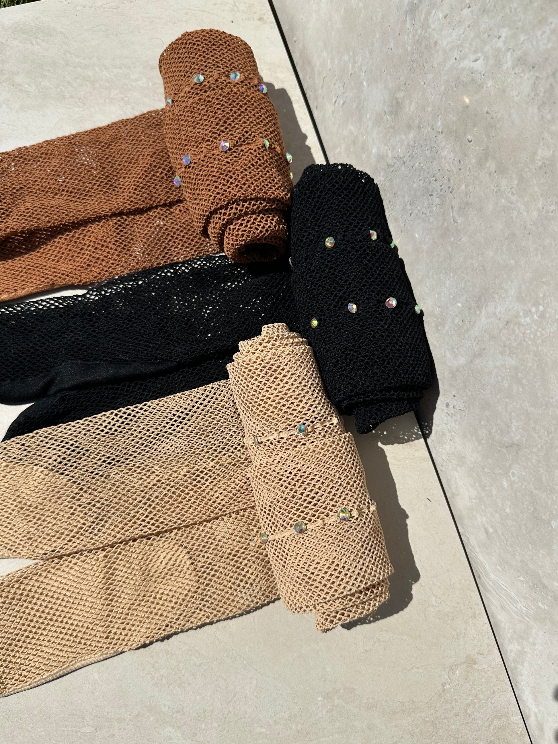3 pairs of fishnet tights with a back seam with diamantés. Tights are rolled up with a dark tan, black and light tan pair of fishnet tights.